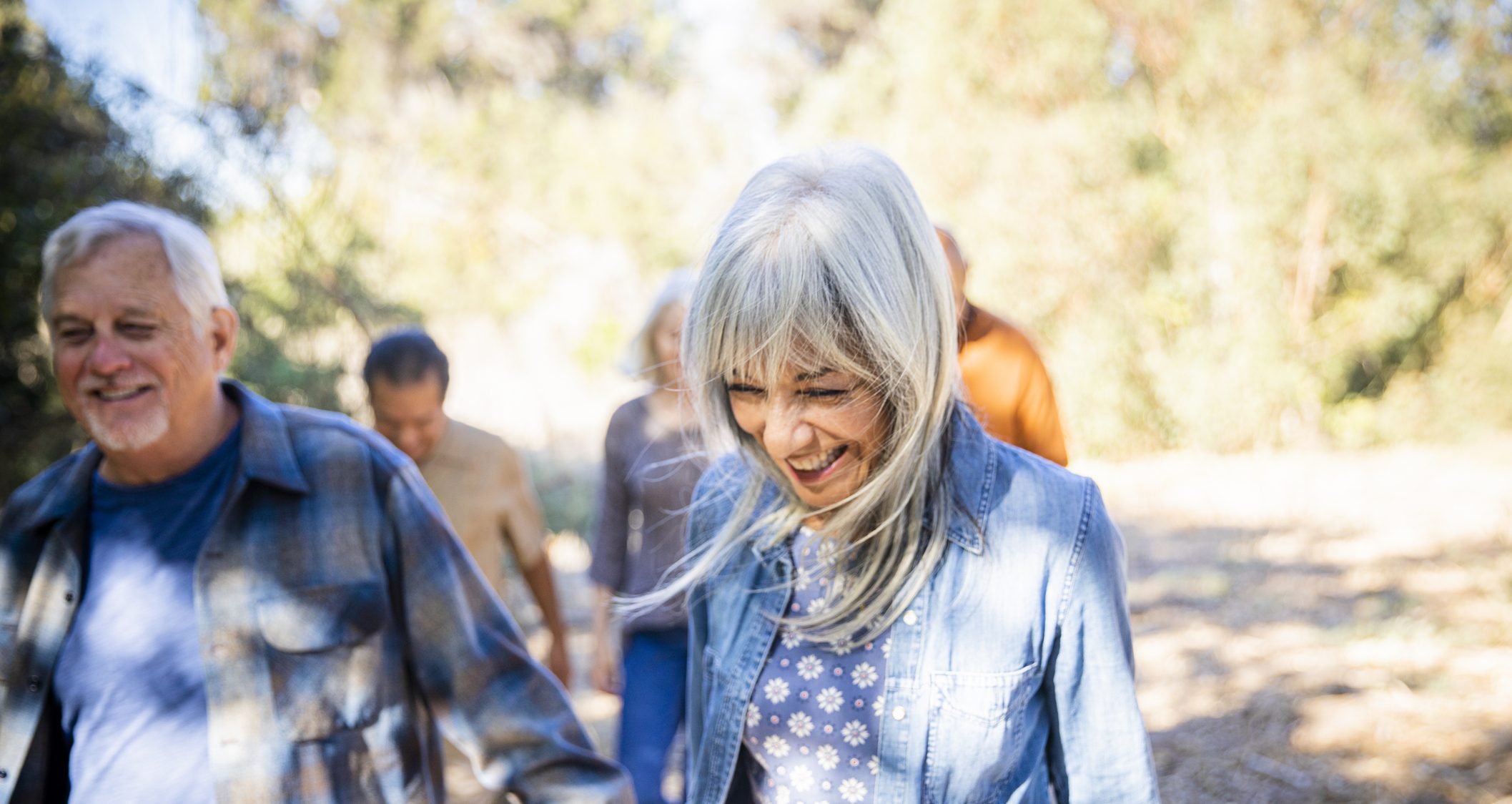 A group of senior friends led by a woman with white hair exploring outdoors.
