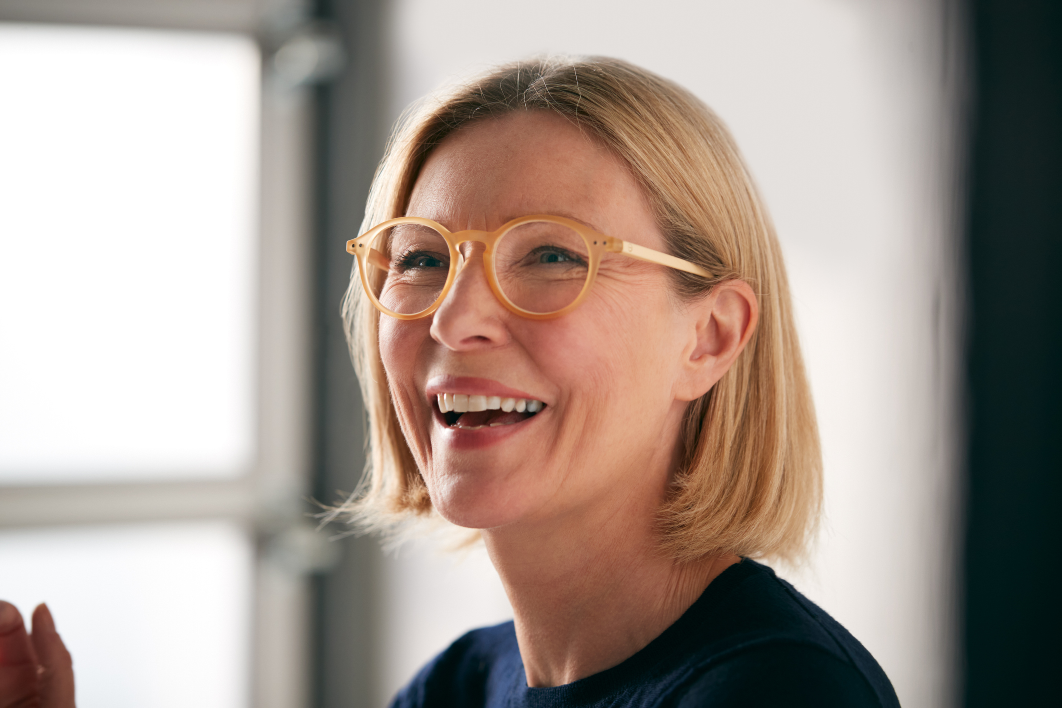 Portrait Of Mature Woman Standing In Front Of Designs On Wall In Start Up Fashion Business